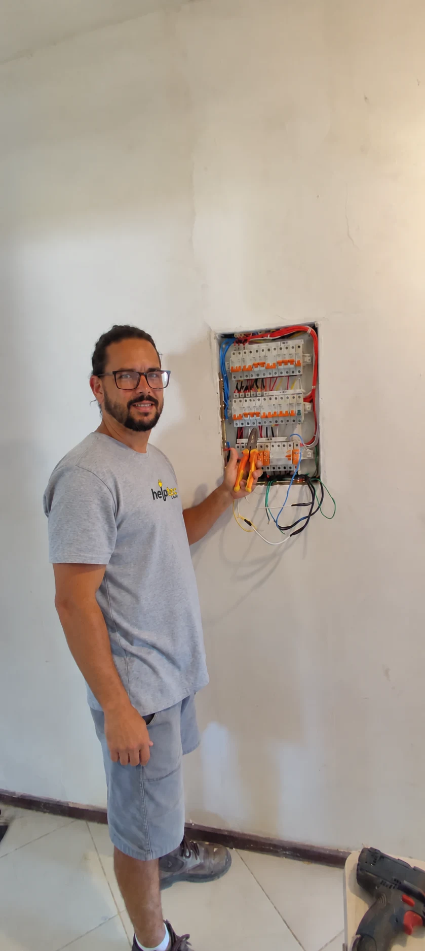 Profissional da Helptec Lagos ao lado de um quadro de disjuntores